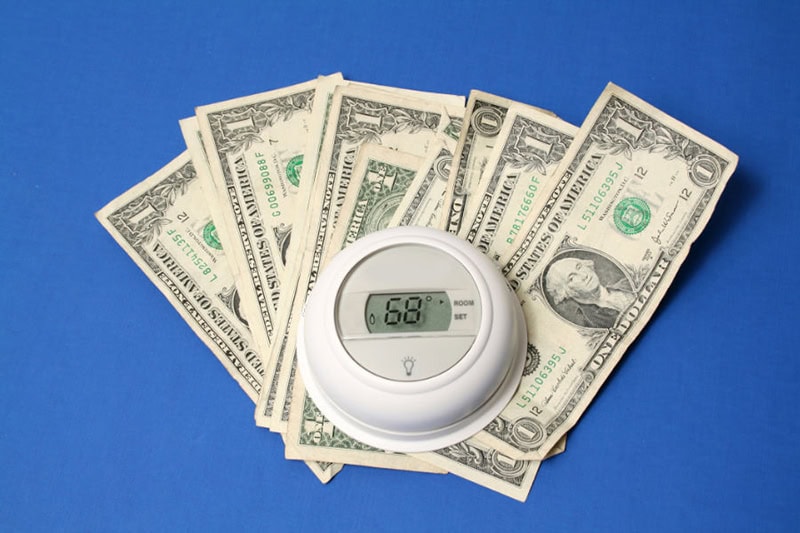Dollar bills underneath an older thermostat to represent spring money-saving tips.
