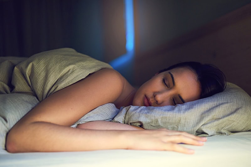 Female homeowner resting peacefully in bed thanks to the health benefits of using your AC while sleeping.