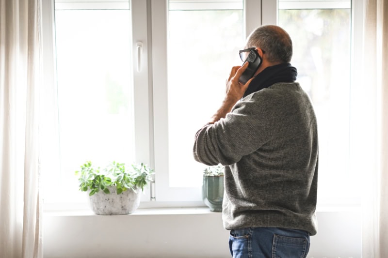 Why Won’t My Furnace Stop Running? Photo of a man looking out of his window talking on the phone.